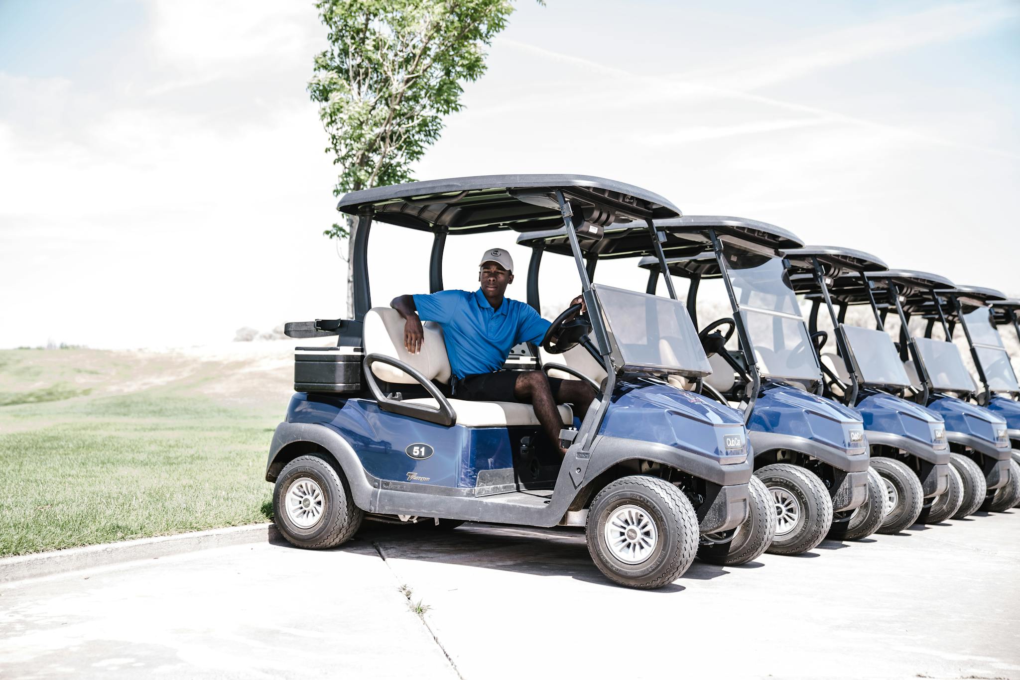 A man sitting in a row of blue golf carts parked on a sunny day.